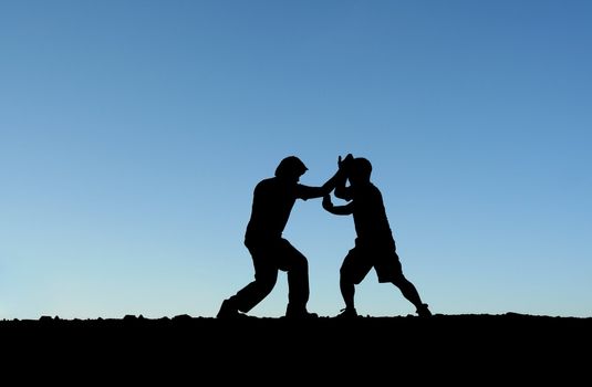 Two men practicing martial arts on top of a mountain (in silhouette)