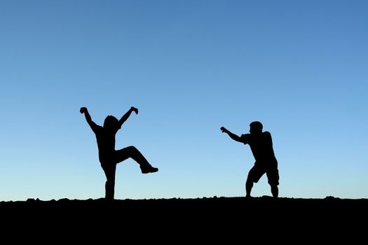 Two men practicing martial arts on top of a mountain (in silhouette)