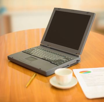 Laptop on a table at office with documents and cup