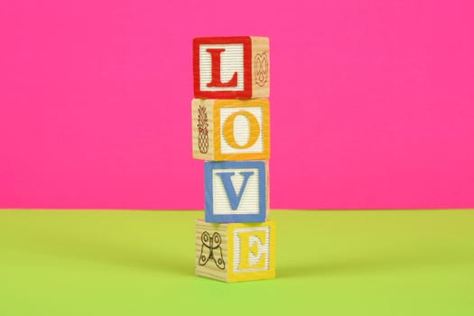 The word love spelled in childrens block with a pink and green background.