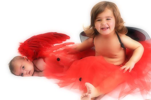 two sisters playing and smiling in studio wearing red angle wings