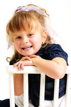 young pretty blond girl with blue dress sitting on a white chair and smiling