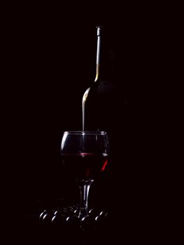 bottle, wineglass, beads on a black background. Studio light.Low key