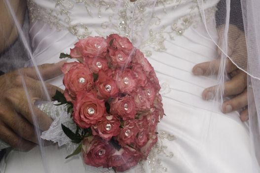 groom standing with his hand wearing a wedding ring and red bouquet on his brides bum
