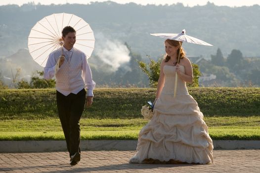 red head sexy beautiful bride and groom walking outside in sun with umbrellas jumping and smiling
