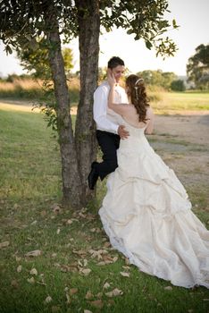 just married couple standing and kissing against a tree in the shade on a sunny day