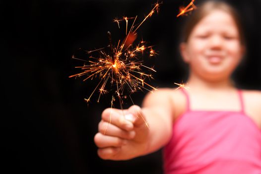 a pretty young girl wearing green polka dot dreass holding a yellow sparkler firework with her hand and smiling