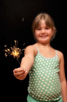 a pretty young girl wearing green polka dot dress holding a yellow sparkler firework with her hand and smiling