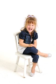 young pretty blond girl with blue dress sitting on a white chair and laughting