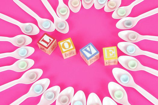 Plastic white spoons make a heart with candy and childrens blocks spell the word love.