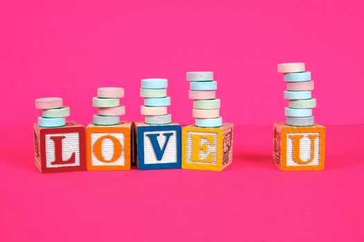Childrens blocks spell the words love you with bright colors, pink background and stacked candy.