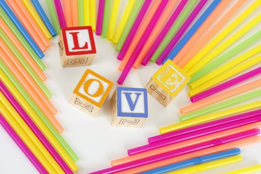 Colorful Straws make a heart shape and childrens bloks spell the word Love.