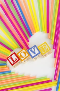 Colorful Straws make a heart shape and childrens bloks spell the word Love.