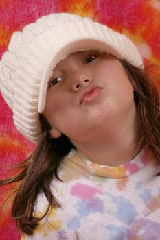 Young girl making a funny fishy or kissy face with knit hat and pink background.