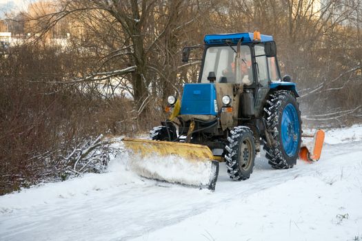 A blue tractor driving down a snow covered UK road during the winter snowfall in  2010. The tractor driver is unrecognizable