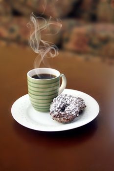 Coffe and donuts on a white plate with steam rising up from the cup.