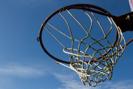 Basketball hoop, rusty ring and broken rope netting set against a blue sky.