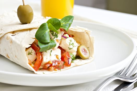 Lavash with a cheese filling, tomato, spinach, olives and a glass of juice.
