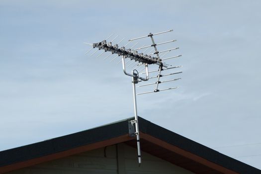 Aluminium T.V. arial with fanned receivers fixed to a pole attached with a bracket to a wooden roof.