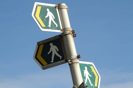 A post containing three public footpath signs depicted by a person in white on a green background with a yellow directional arrow.
