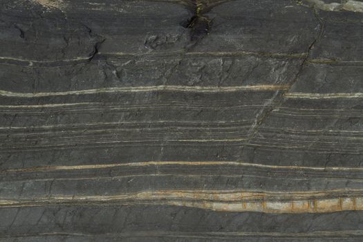 Dark grey rock shot with light coloured quartz crystal streaks on a horizontal plane.