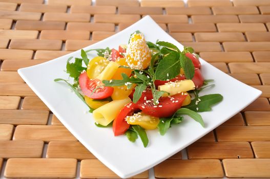 Salad of red and yellow tomato with cheese, arugula, sesame