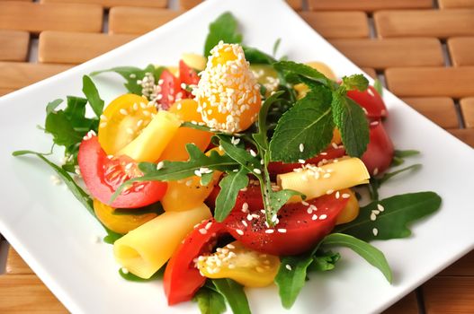 Salad of red and yellow tomato with cheese, arugula, sesame