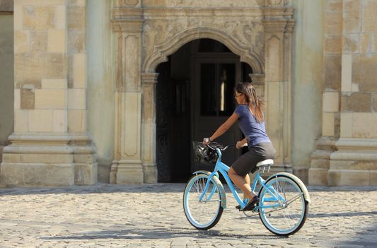 Brunette woman riding a bicycle in an old city square in a hot summer day.