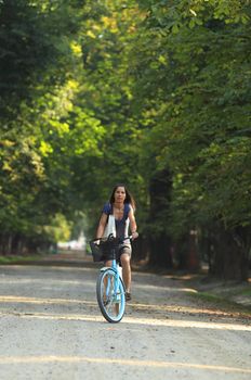 Young woman riding a bicycle in a park alley. 