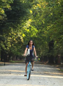 Young woman riding a bicycle in a park alley. 