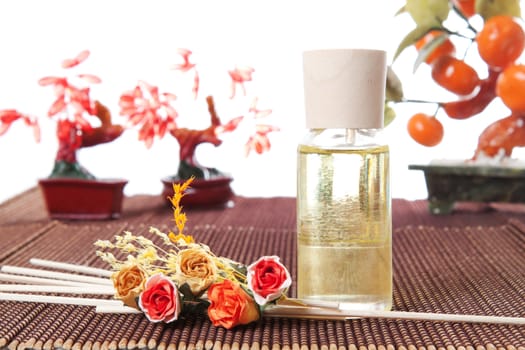 Glass bottle with yellow oil and small flowers lay on brown mat. Stone trees at the background