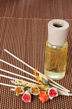 Glass bottle with yellow oil and small flowers lay on brown mat