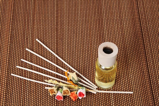 Glass bottle with yellow oil and small flowers lay on brown mat