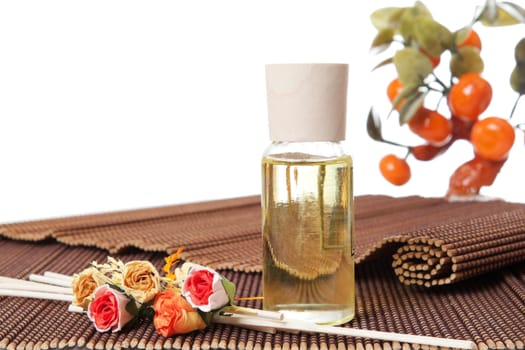 Glass bottle with yellow oil and small flowers lay on brown mat. Stone trees at the background