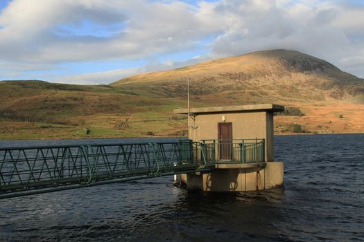 Water storage facility, a reservoir, under a hill. a bridge leads to the access building.