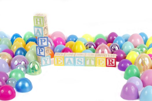 Childrens blocks spell Happy Easter with colorful plastic eggs on a white background.