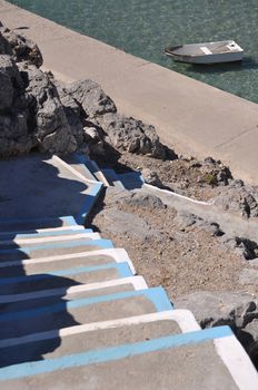 traditional white and blue stairway in a Pserimos greek island (focus on the boat)