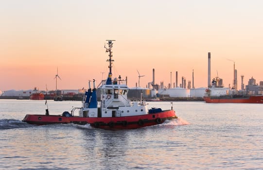 Tug passing by at high speed on the river at colorful sunset - industrial pollution is painting the sky 