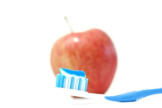 A Toothbrush with Toothpaste and an apple in the Background