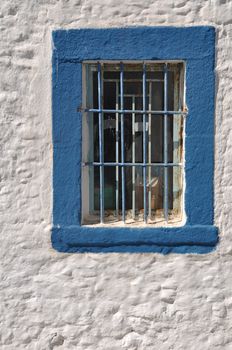 blue window with bars on white house in Greece