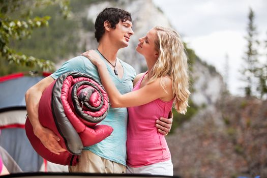 Young woman carrying sleeping bag and embracing woman while camping