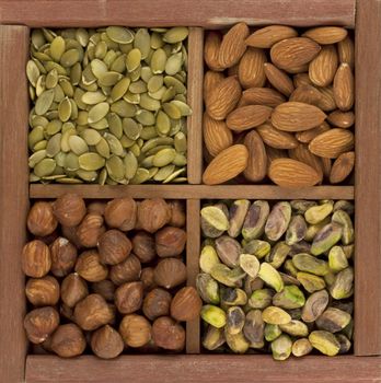 four healthy raw snacks, almonds, hazelnuts, pistachio nuts and pumpkin seed, in a rustic wooden box or drawer with dividers