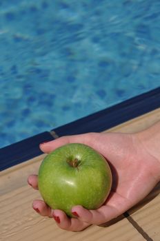 woman holding a green apple at the pool side as a diet concept