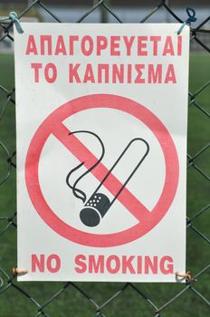 forbidden to smoke sign hanging on a sports court fence (greek and english language)