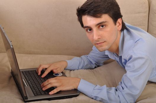 attractive young man with laptop computer lying on the couch at home