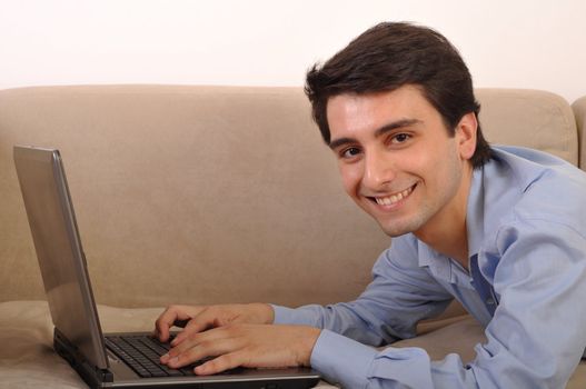 attractive young man with laptop computer lying on the couch at home