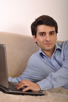 attractive young man with laptop computer lying on the couch at home