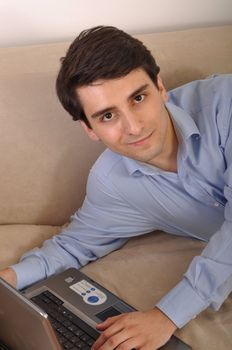 attractive young man with laptop computer lying on the couch at home