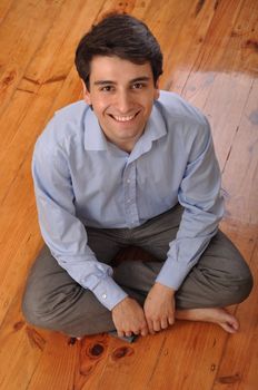 smiling attractive young man sitting on wooden floor at home