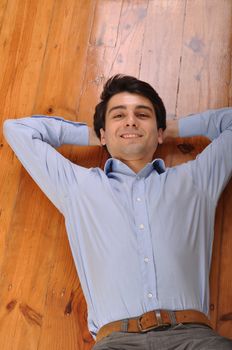 smiling attractive young man lying on wooden floor at home